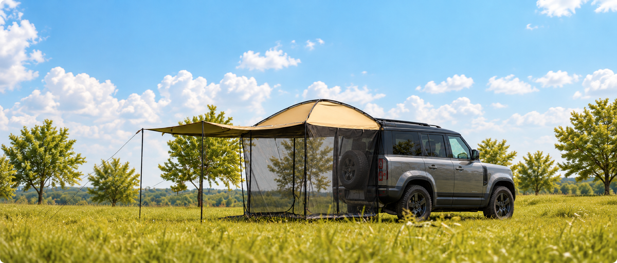 AT200 rear-mounted tent and extended shade beside a gray Defender in a sunny meadow